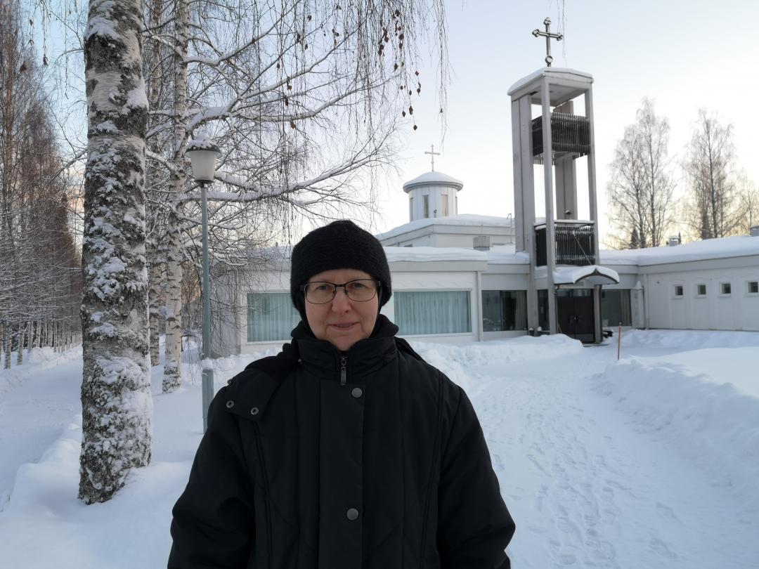 Nunna Ksenia seisoo taustallaan näkyvän Lintulan luostarin pihassa talvella