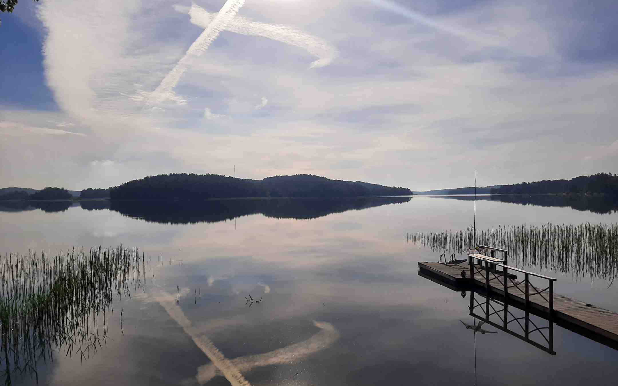 Suihkukoneiden juovat muodostavat taivaalle ristin, joka heijastuu järven pintaan