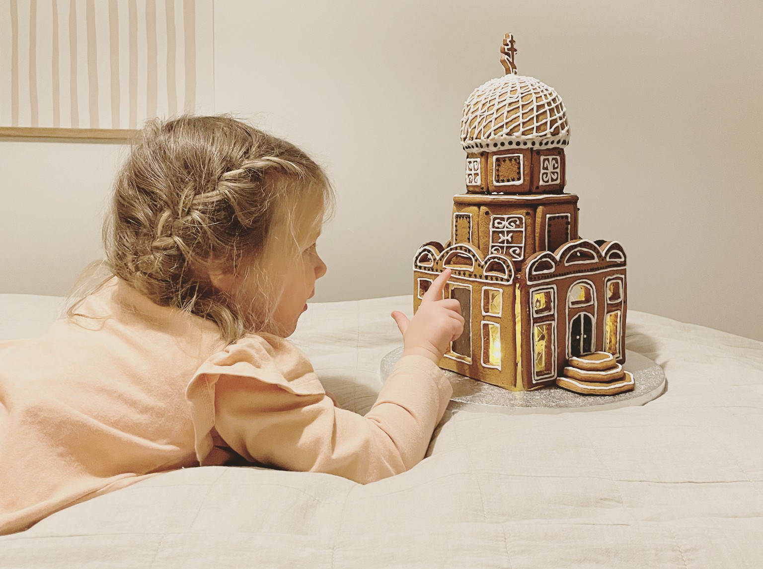 Pieni tyttö makaa vatsallaan ja tutkii piparkakkukirkkoa