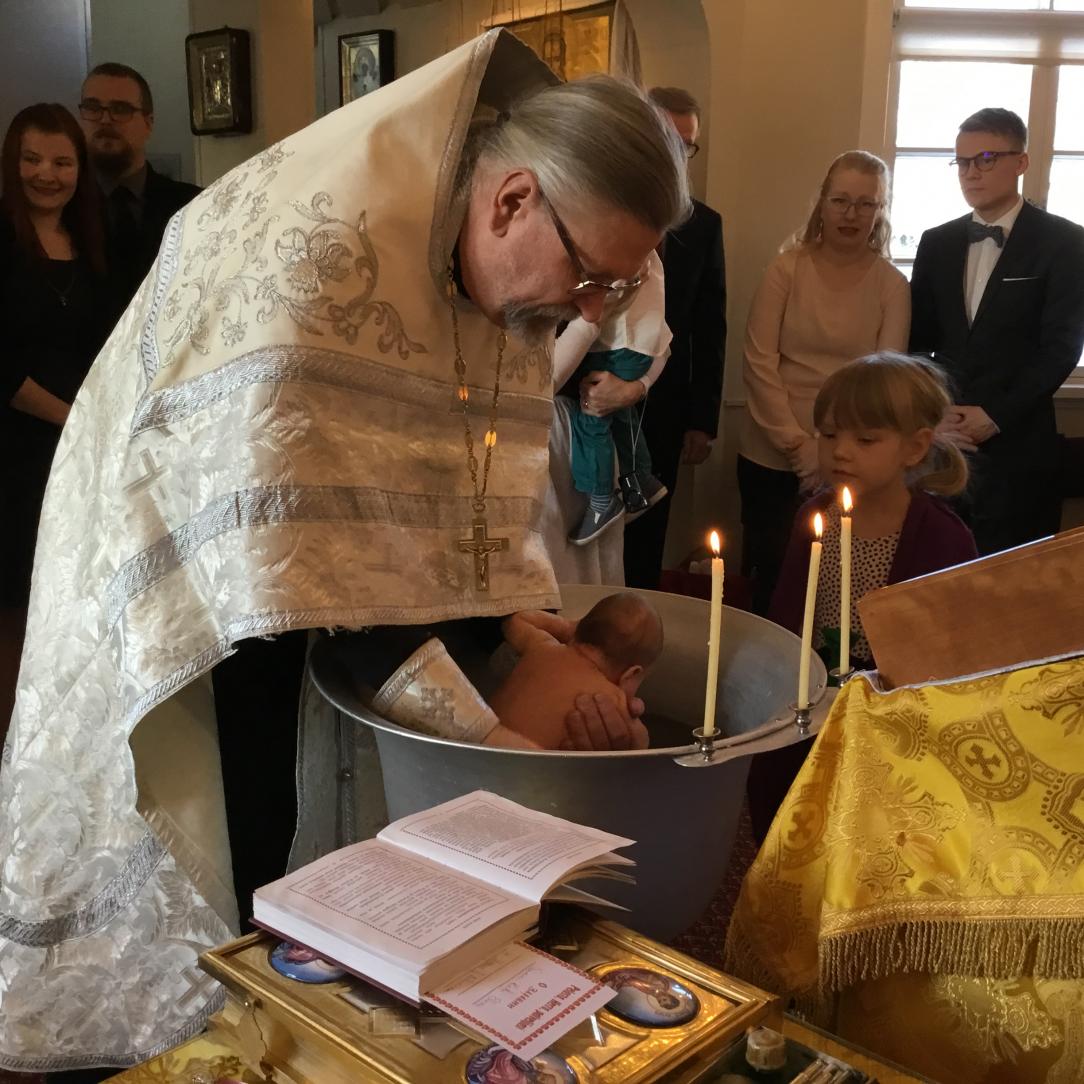 Ortodoksipappi kastaa lapsen upotuskasteella