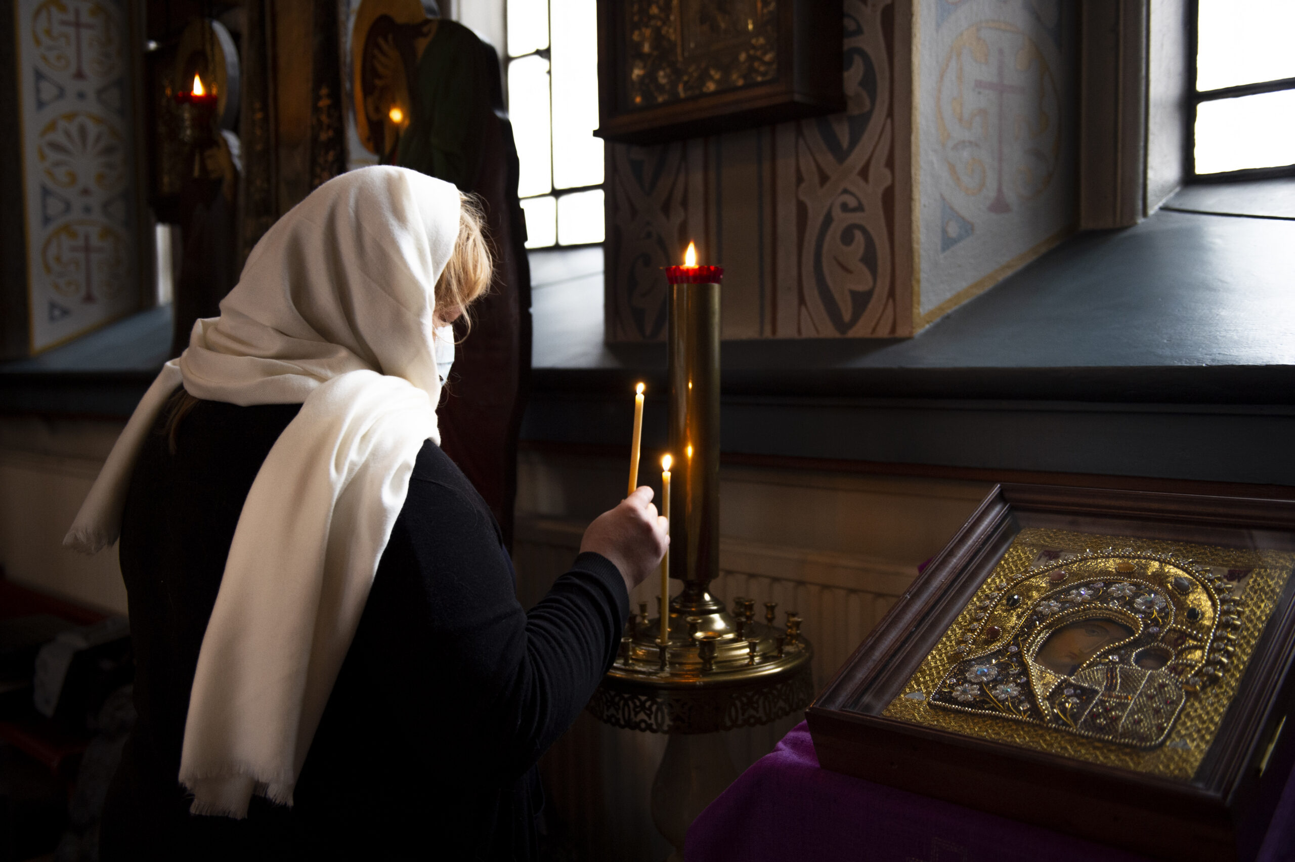 Valkoisella huivilla päänsä peittänyt ortodoksinainen sytyttää tuohuksen Jumalanäidin ikonin edessä