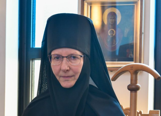 Lintulan luostarin igumenia Ksenia seisomassa ikonin edessä igumenian sauva kädessään 2023